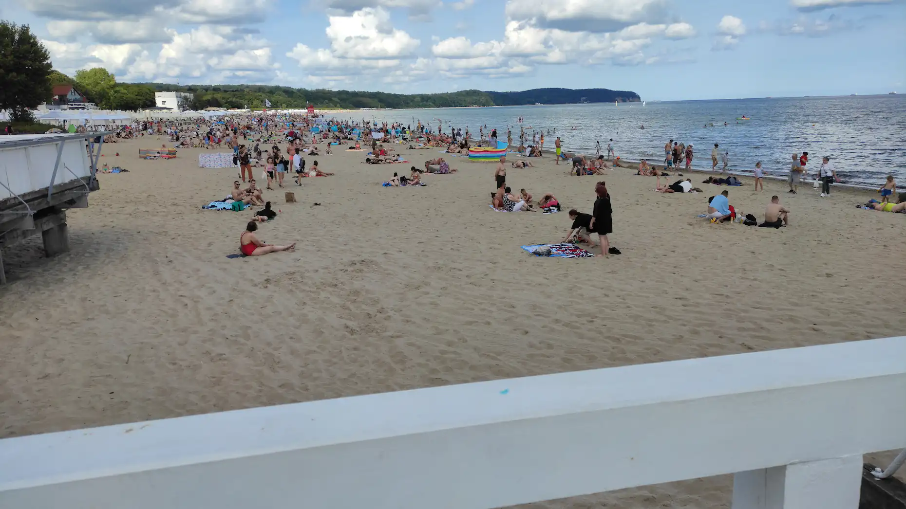 Sopocka plaża w sierpniowe południe, koce i parawany na piasku, w tle zatoka i cypel